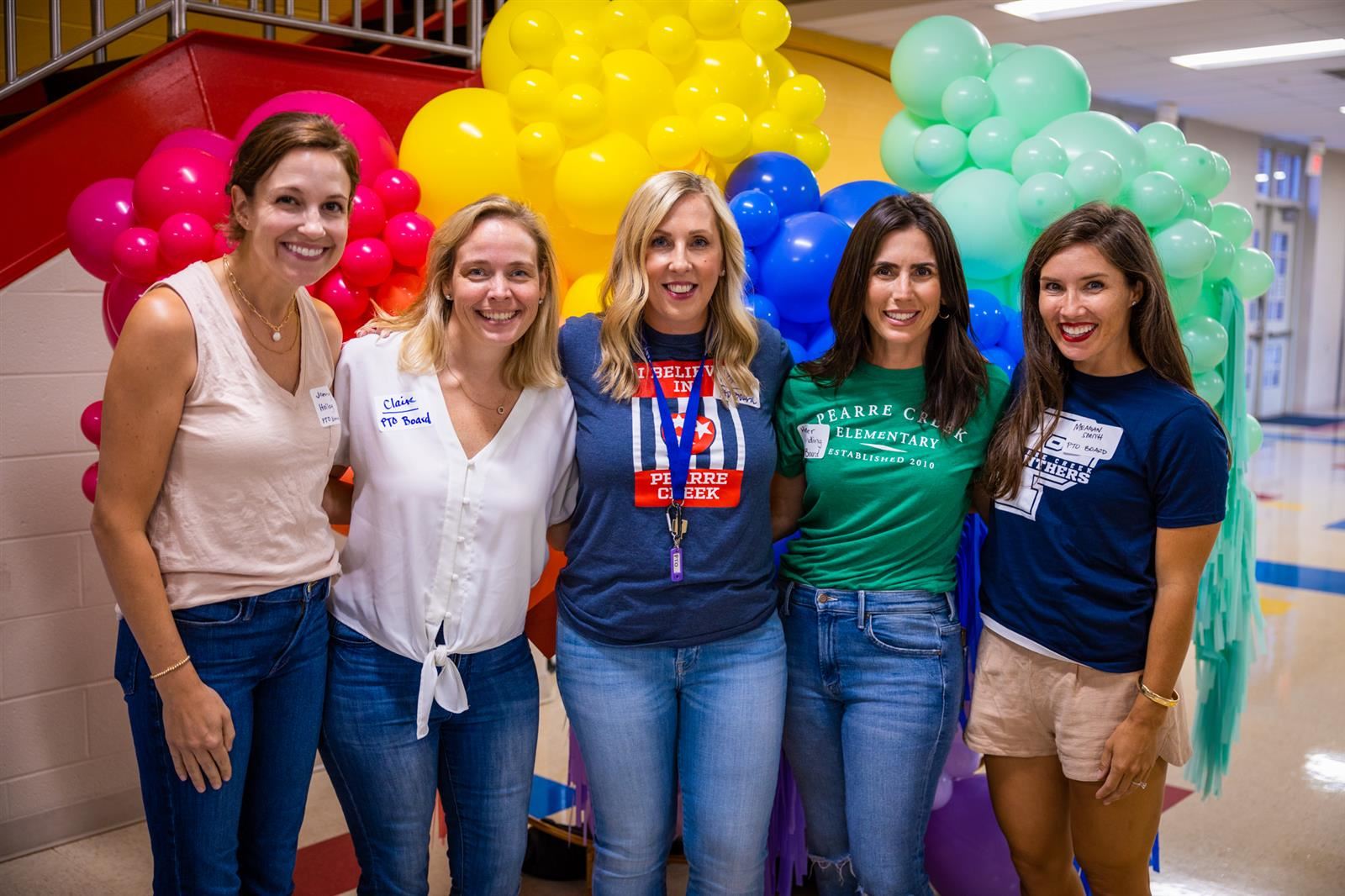 Five PTO volunteer ladies standing in front of a colorful balloon display.